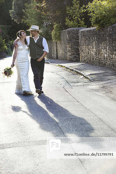 Braut und Bräutigam gehen eine ländliche Straße entlang.