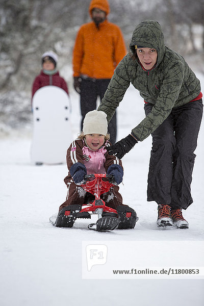 Mother assisting girl while riding on sledge on snow