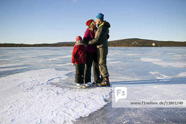Eltern mit Tochter beim Schlittschuhlaufen auf dem zugefrorenen See