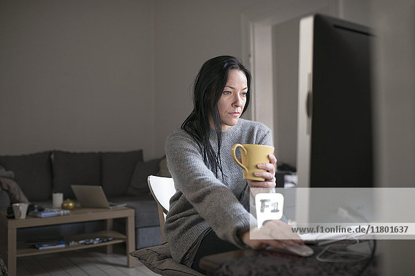 Frau hält Tasse und benutzt Computer
