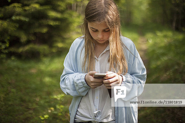Mädchen benutzt Mobiltelefon im Wald