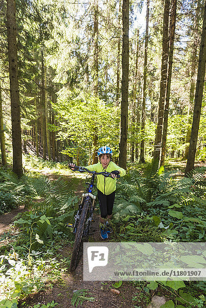 Boy pushing bike through forest