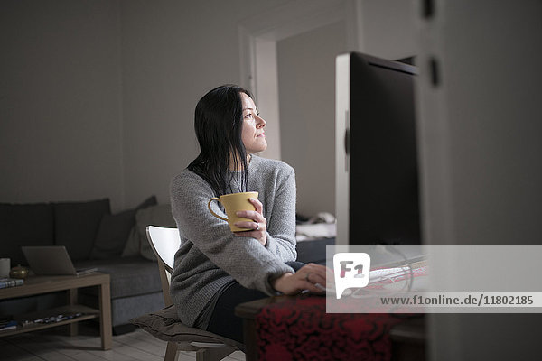 Woman holding mug sitting by computer