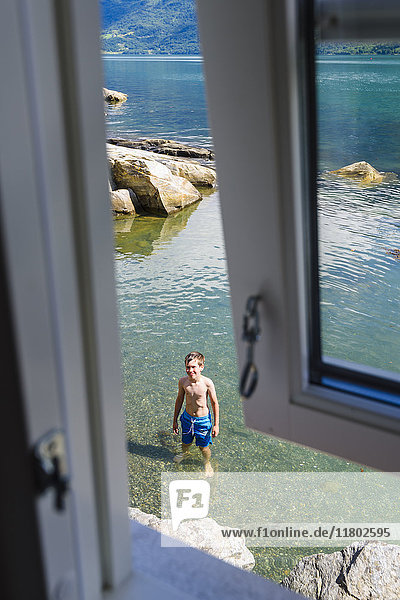 Junge im Meer stehend vom Fenster aus gesehen