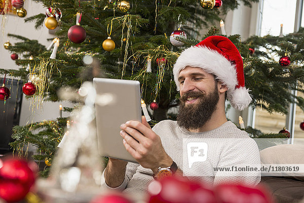 Junger Mann mit digitalem Tablet und Weihnachtsmannmütze