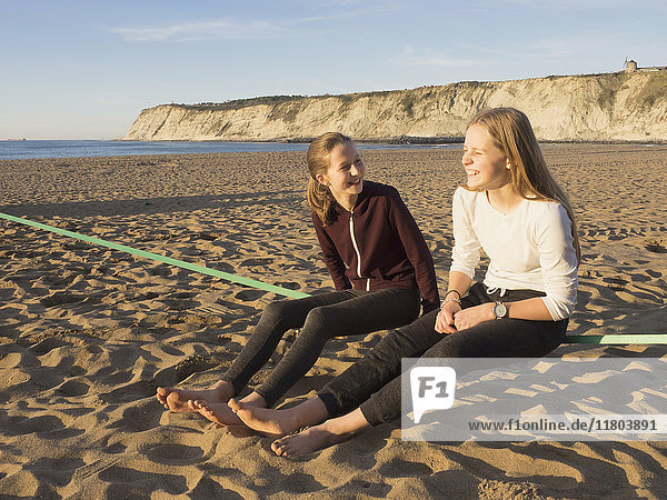 Teenager-Mädchen sitzen auf einer Slackline an einem Strand in Nordspanien