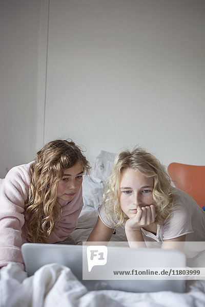 Two teenage girls using laptop in bedroom
