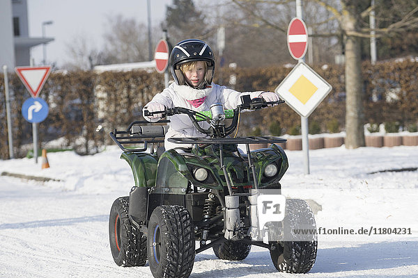 Mädchen fährt Quad auf schneebedeckter Straße