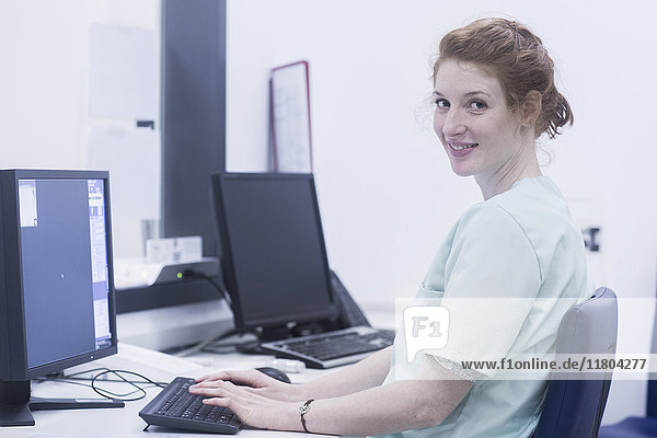 Lächelnde Krankenschwester  die an einem Computer arbeitet  während sie am Krankenpflegeplatz sitzt