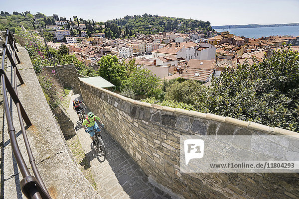 Biker klettern auf gepflasterten Oberfläche von Steinmauer mit Häusern im Hintergrund
