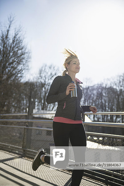 Woman in sportswear holding water bottle and jogging
