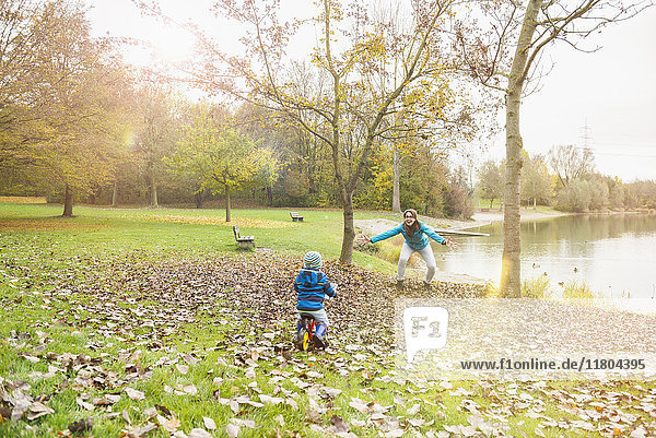 Little boy driving with his walking bicycle towards his mother in autumn scenery