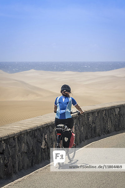 Rear view of woman cycling on road by sand dune and sea