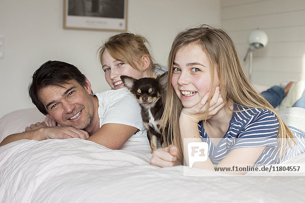 Vater mit Töchtern und Hund auf dem Bett