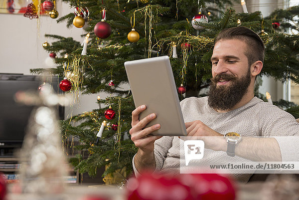 Junger Mann mit digitalem Tablet gegen Weihnachtsbaum