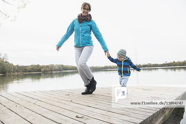 Smiling mother with son walking on wooden jetty over lake