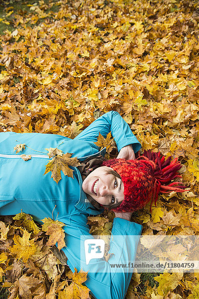 Lächelnde Frau auf dem Boden liegend in einem Haufen von Herbstblättern