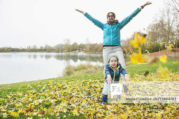 Mother and son throwing autumn leaves in air in front of lake