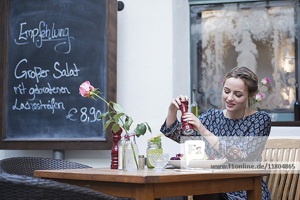 Young woman crushing pepper on salad at cafe by chalkboard