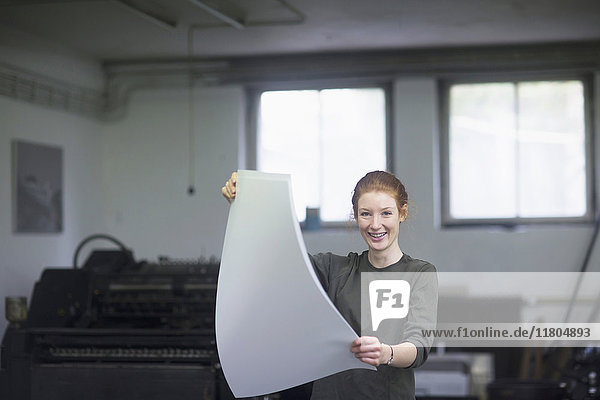 Junge Frau hält ein Bündel Papier an einer Druckerpresse