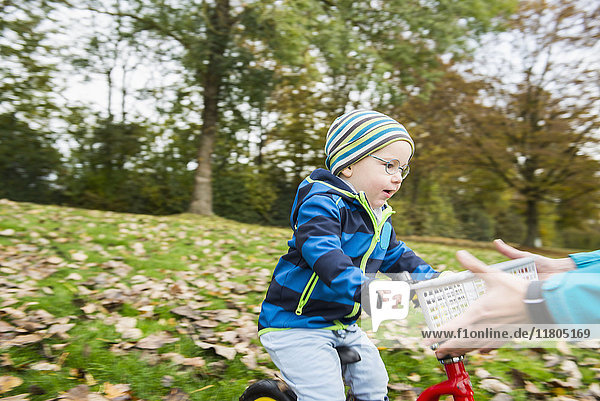 Little boy driving with his walking bicycle towards arms of mother in autumn scenery