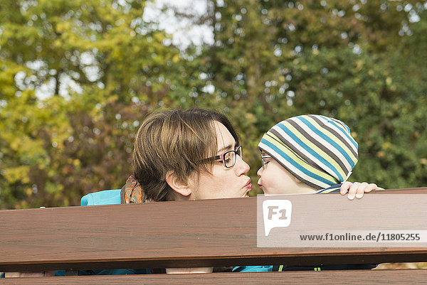 Mutter und Sohn küssen sich hinter der Rückenlehne der Parkbank in der Herbstlandschaft