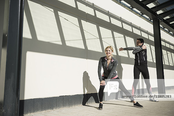 Man and woman in sportswear doing stretching on city footpath