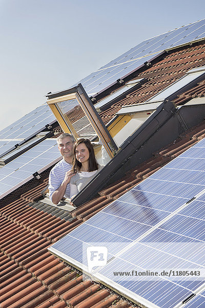 Ehepaar schaut aus einem Dachfenster mit Sonnenkollektoren