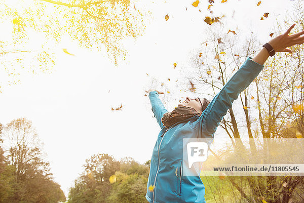 Frau lachend beim Werfen von Herbstblättern in die Luft