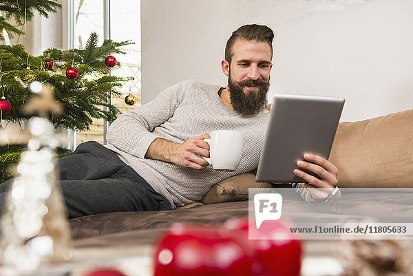Mann benutzt digitales Tablet und trinkt zu Hause Kaffee