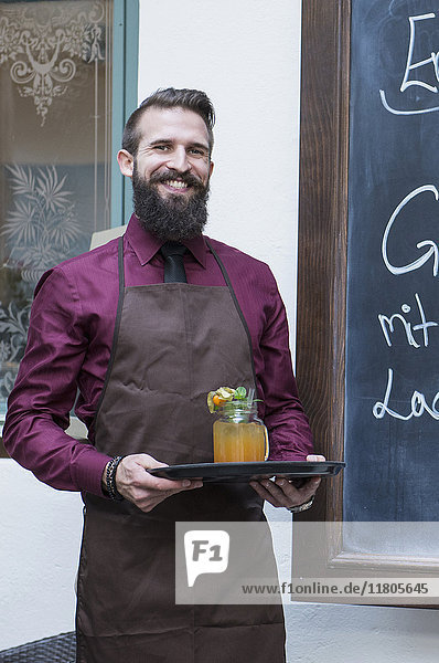 Smiling young man holding mocktail on tray