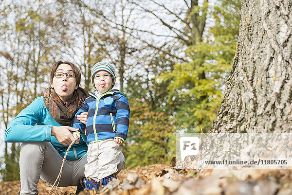 Porträt von Mutter und Sohn mit herausgestreckter Zunge an einem großen Baumstamm im Herbst