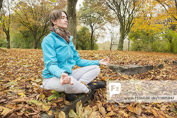 Frau meditiert im Lotussitz auf einem Felsen sitzend in einer Herbstlandschaft