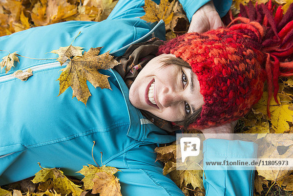 Nahaufnahme einer lächelnden Frau  die in einem Haufen Herbstblätter auf dem Boden liegt