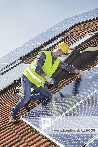 Ingenieur  der Sonnenkollektoren auf dem Dach eines Hauses anbringt