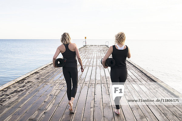 Two women carrying exercise mats  walking on pier