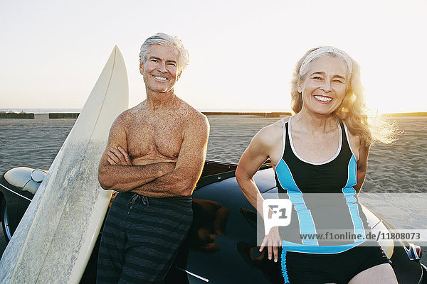 Älteres kaukasisches Paar lehnt sich mit Surfbrettern an ein Cabrio