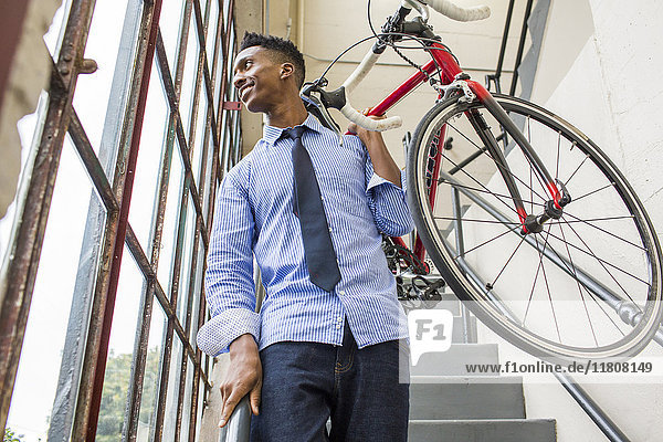 Black businessman descending staircase carrying bicycle