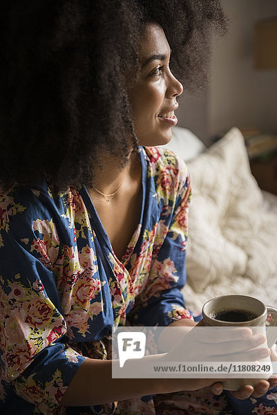 African American woman sitting in bed drinking coffee