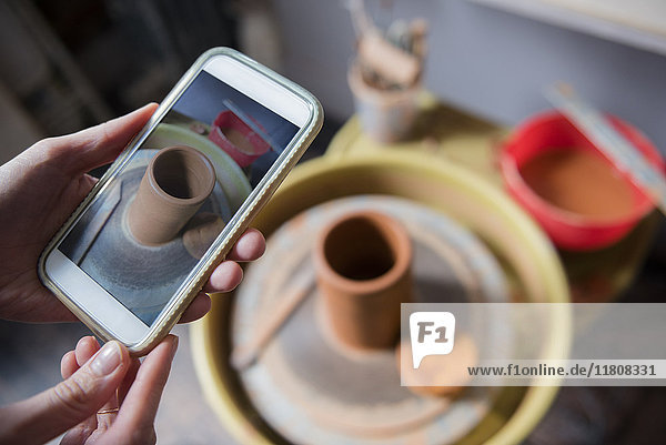 Hands of Caucasian woman photographing pottery with cell phone