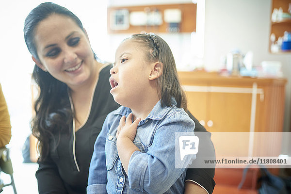 Hispanische Mutter beobachtet Tochter mit Down-Syndrom  die auf den Hals zeigt