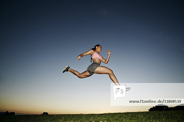 Gemischtrassige Frau läuft und springt im Feld bei Sonnenuntergang
