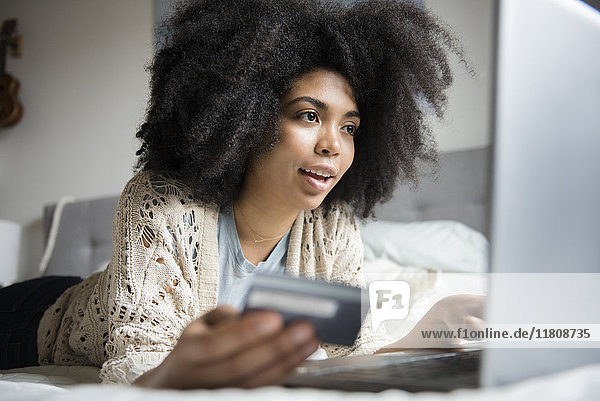 Im Bett liegende afroamerikanische Frau beim Online-Shopping mit Laptop