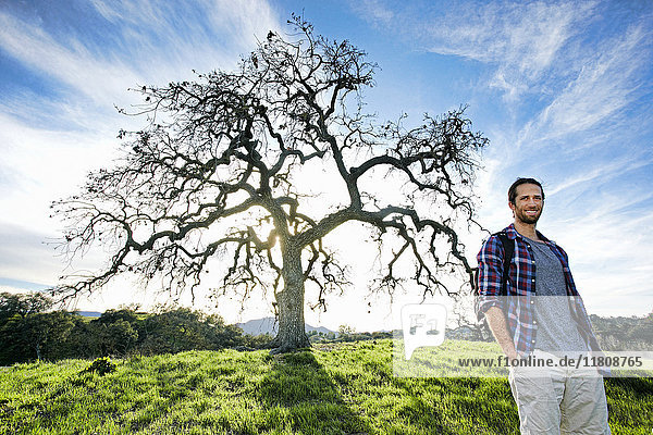 Smiling Caucasian man standing in field near tree