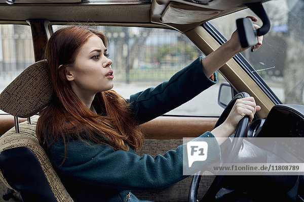 Kaukasische Frau fährt Auto und stellt den Spiegel ein