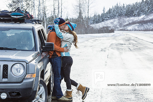 Kaukasisches Paar küsst sich in der Nähe des Autos im Winter
