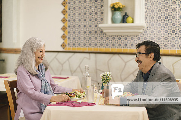 Lächelndes älteres Paar isst Salat und lacht im Restaurant