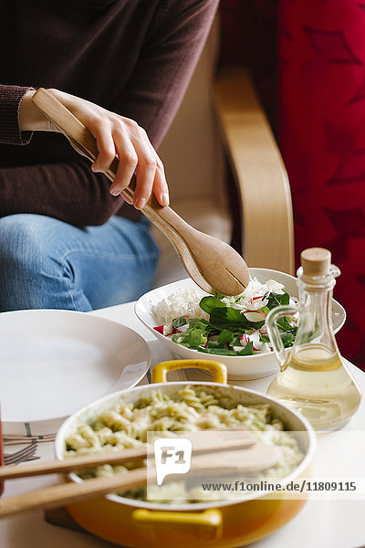 Frau serviert Salat mit einer Holzzange