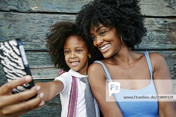 Smiling mother and daughter posing for cell phone selfie