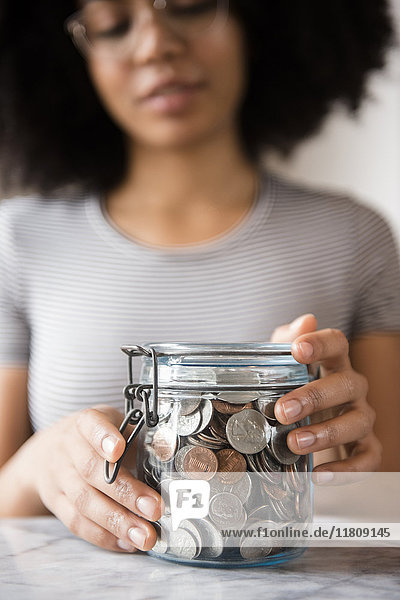 Lächelnde afroamerikanische Frau mit einem Glas voller Münzen